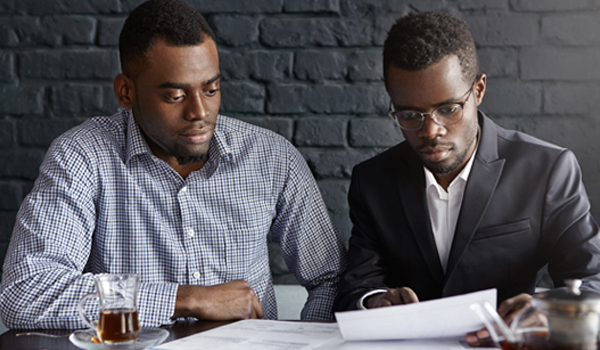 Two young African-American executives reviewing financial report: worried male in spectacles holding piece of paper, showing something in document to his colleague, both having frustrated looks
