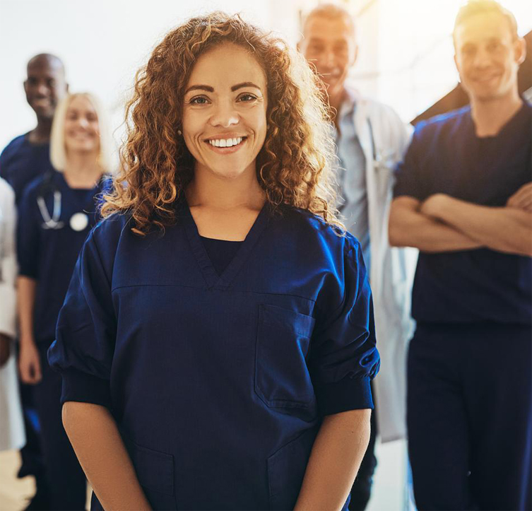 Smiling young female doctor standing in a hospital corridor with a diverse group of medical staff standing behind her
